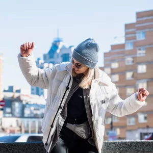 Joven estudiante con chaqueta blanca y gorro gris disfrutando en una ciudad moderna